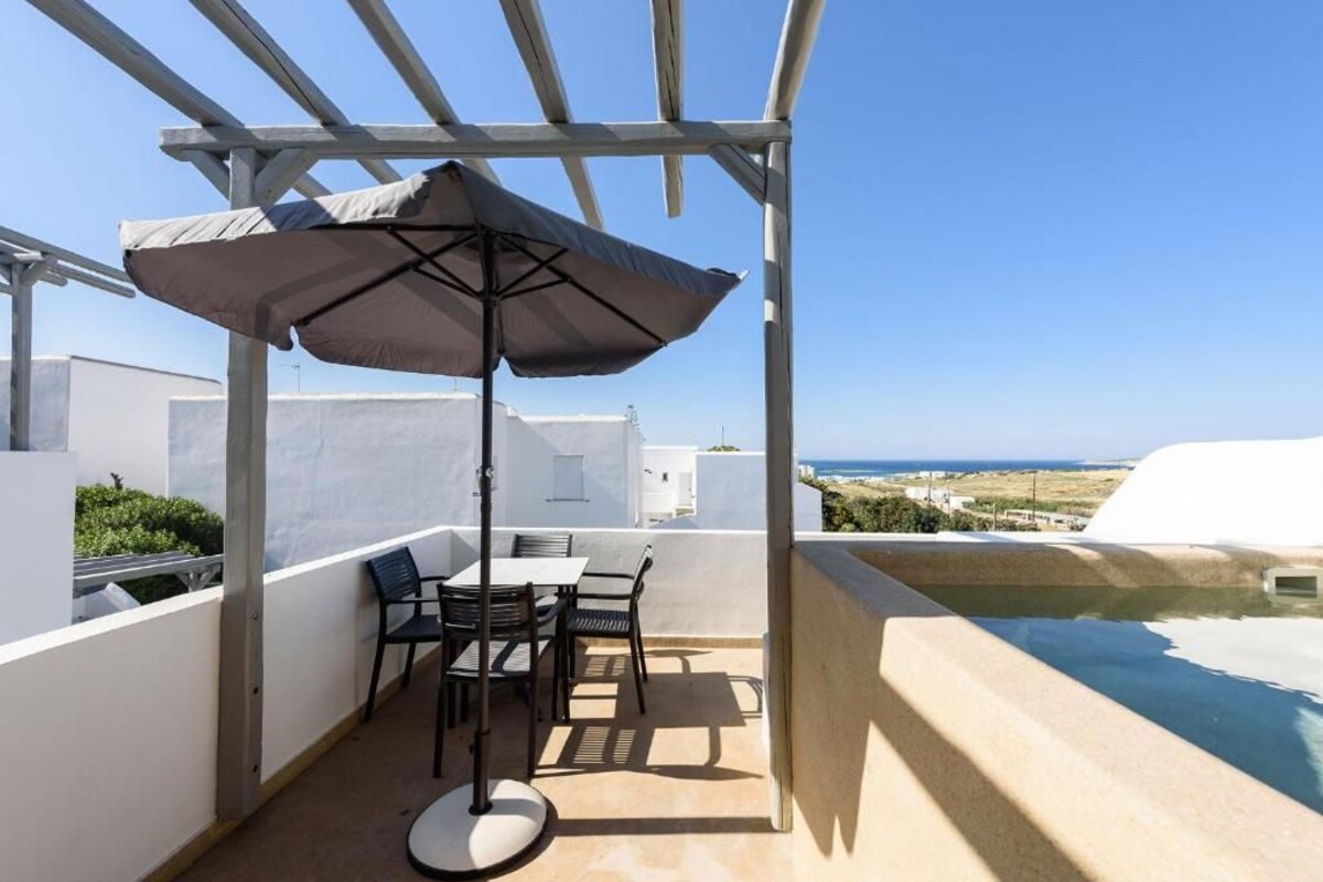 A patio with a table and chairs, an umbrella, and a view of the sea.