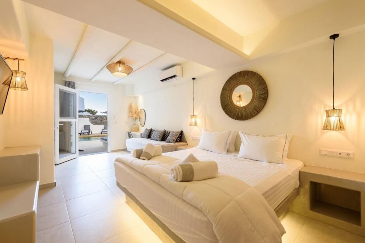 A bedroom with a large bed, a round mirror, and a view of the outside.