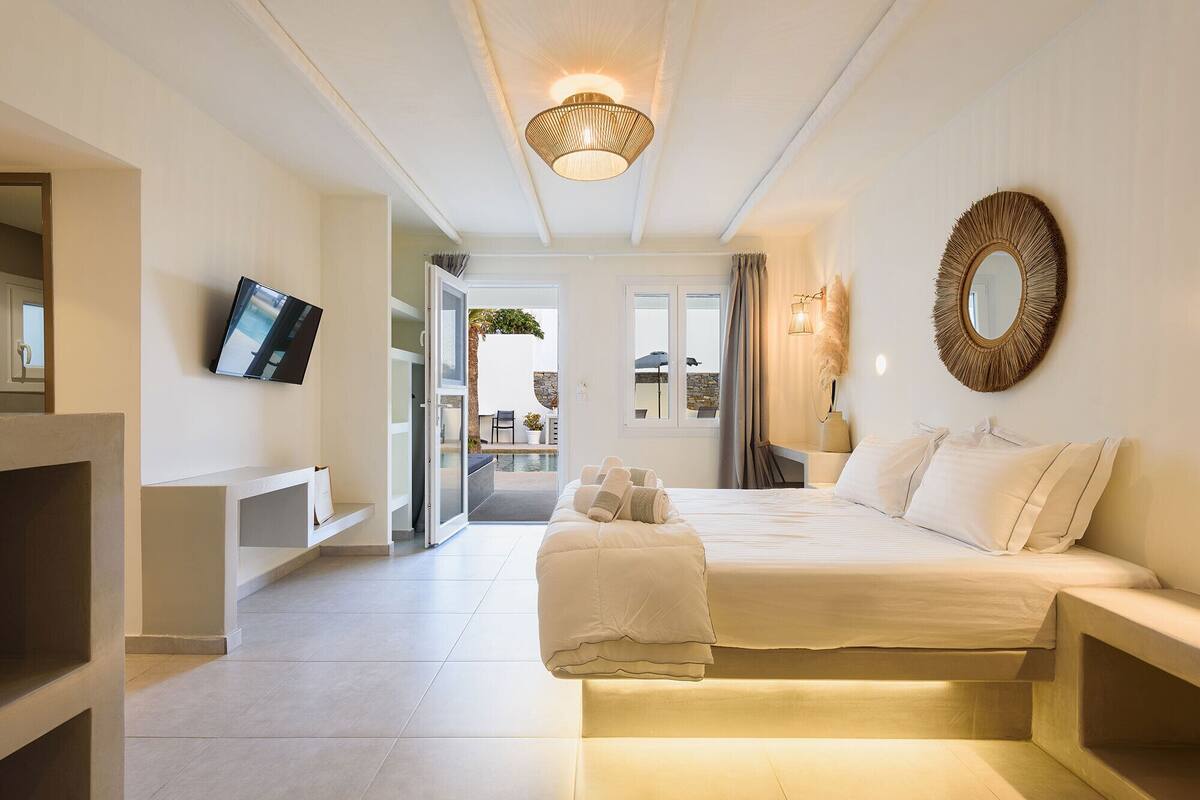 A modern bedroom with a bed, a TV, and a view of the outdoor area.