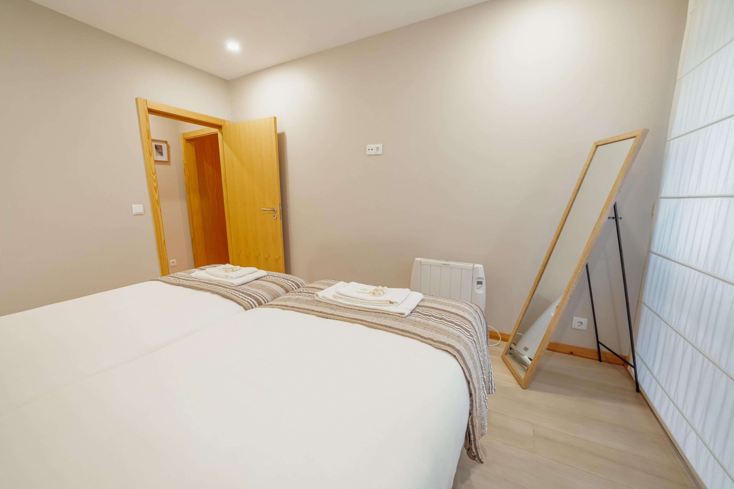 Un dormitorio con una cama, una puerta de madera, un radiador y un espejo apoyado contra la pared.