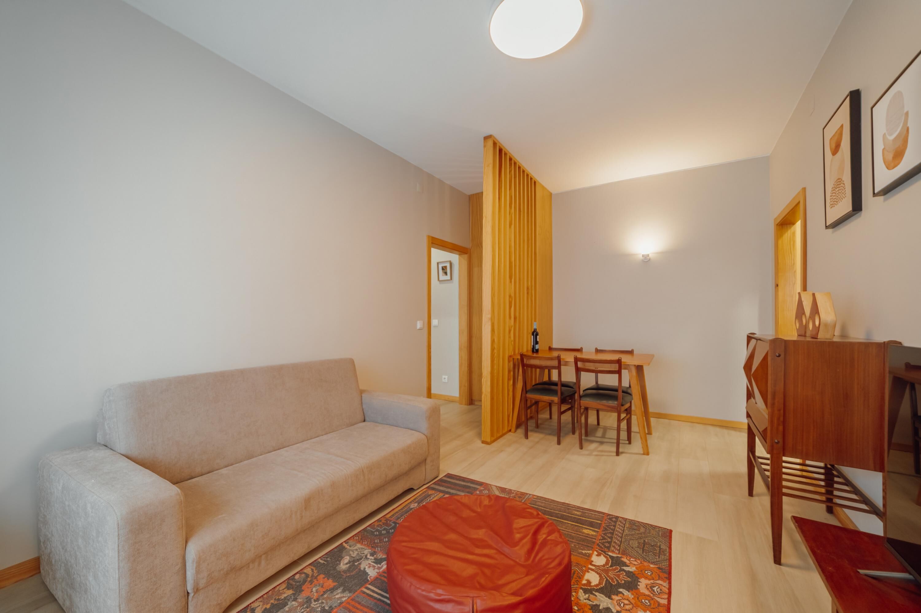 A living room with a sofa, a dining table with chairs, a wooden partition, and a small table with a bottle.