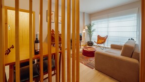 A modern living room with a sofa, a dining table with chairs, a red ottoman, and a large window with sheer curtains. - Good Morning Apartment With Garage by Vacationy (Porto)