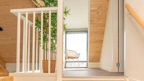 Una escalera de madera con barandilla blanca que conduce a un balcón con una silla de mimbre y plantas en macetas.