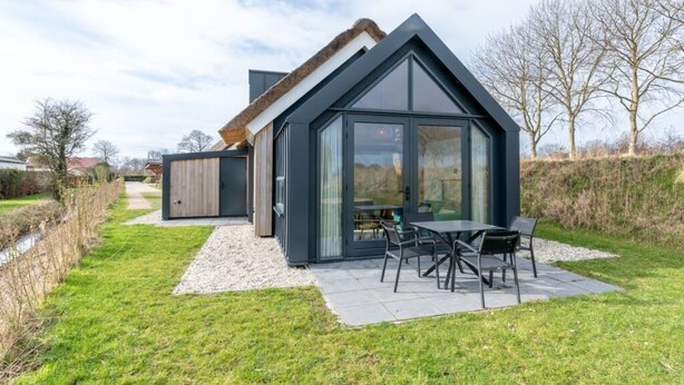 Una casa moderna con un amplio ventanal, un patio con mesa y sillas, y una zona verde.