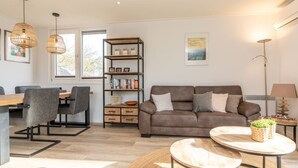 Ein modernes Wohnzimmer mit einem braunen Ledersofa, zwei grauen Sesseln, einem Holztisch und einem Bücherregal.