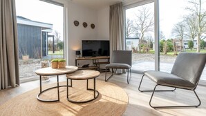 Ein modernes Wohnzimmer mit Fernseher, zwei kleinen Tischen und einem großen grauen Sessel.