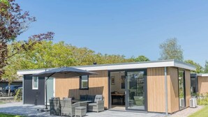 Ein modernes Haus mit Terrasse, Sitzgelegenheiten im Freien und einem großen Glasbalkon.