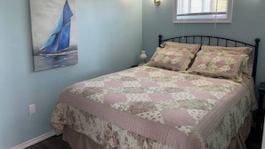 A bedroom with a bed, a painting, a window with blinds, and a wall-mounted light fixture.