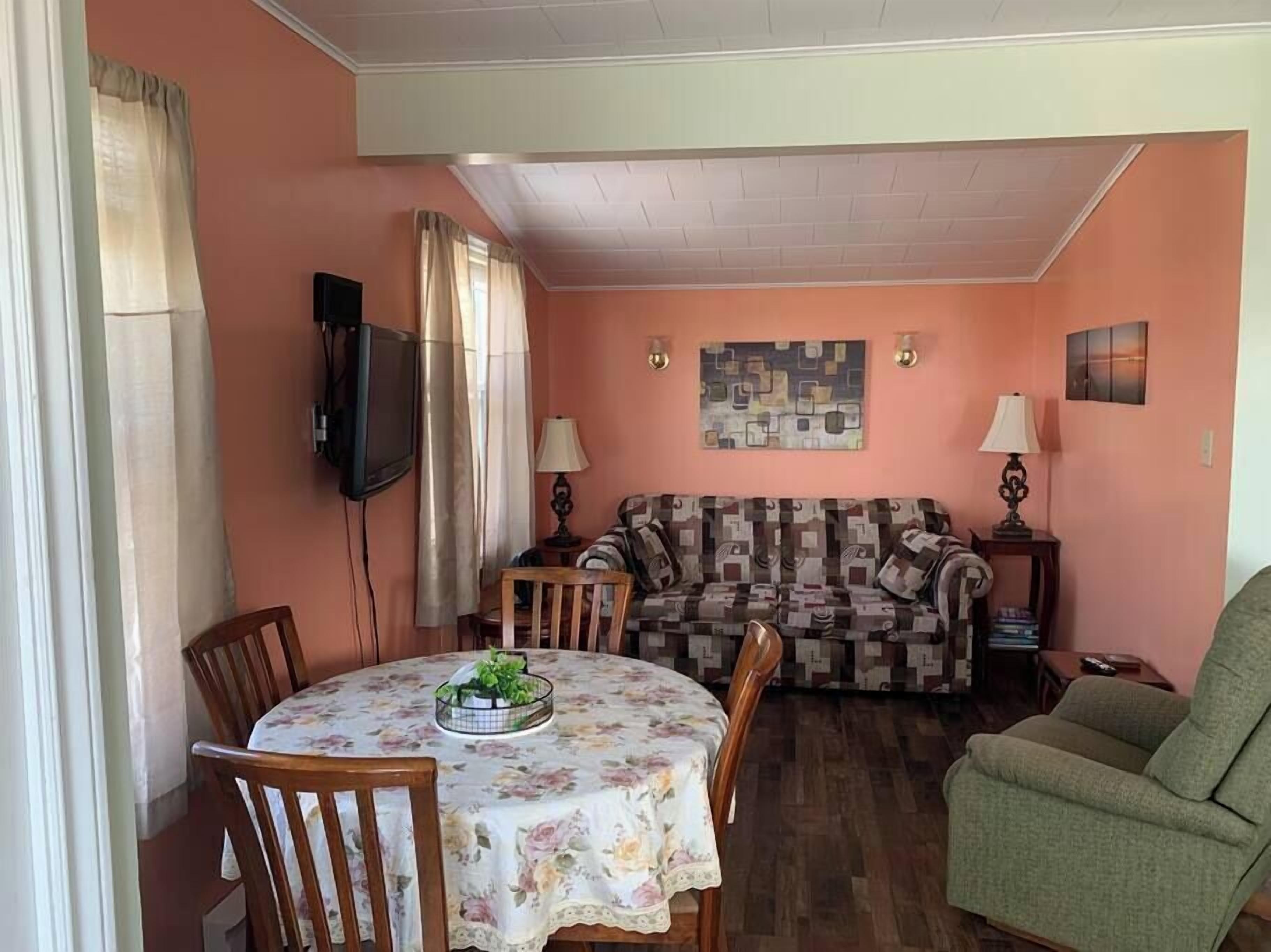 A living room with a sofa, a dining table with chairs, a television, and a lamp.