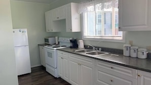 A kitchen with white cabinets, a stove, a microwave, a sink, and a window with blinds.