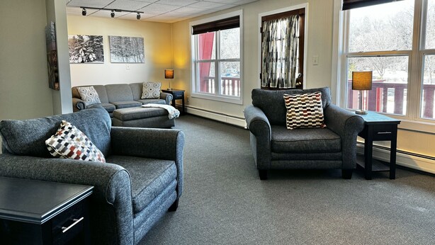A modern living room with grey sofas, a coffee table, and a lamp. There are large windows with curtains and a view of trees. - Cozy 2-Bedroom Upstairs Apartment in  Paradise (Paradise)