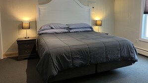 A neatly arranged bedroom with a large bed, two bedside tables with lamps, and a window with blinds. - Cozy 2-Bedroom Upstairs Apartment in  Paradise (Paradise)