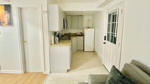 A compact living space with a kitchenette, a grey sofa, and a door leading to another room.