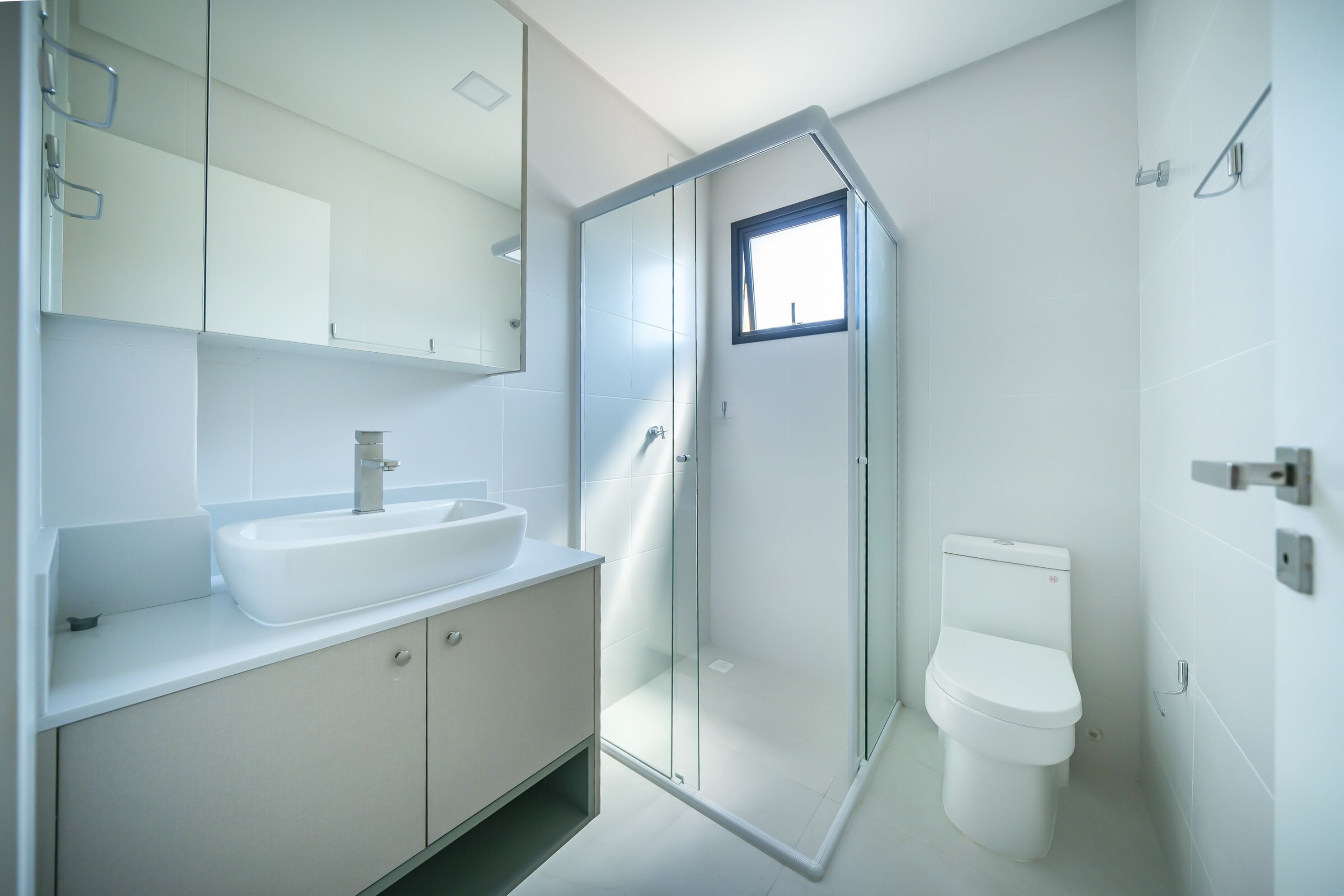 Ein modernes Badezimmer mit einer Glaskabine zur Dusche, einem weißen Waschbecken und einer Toilette.