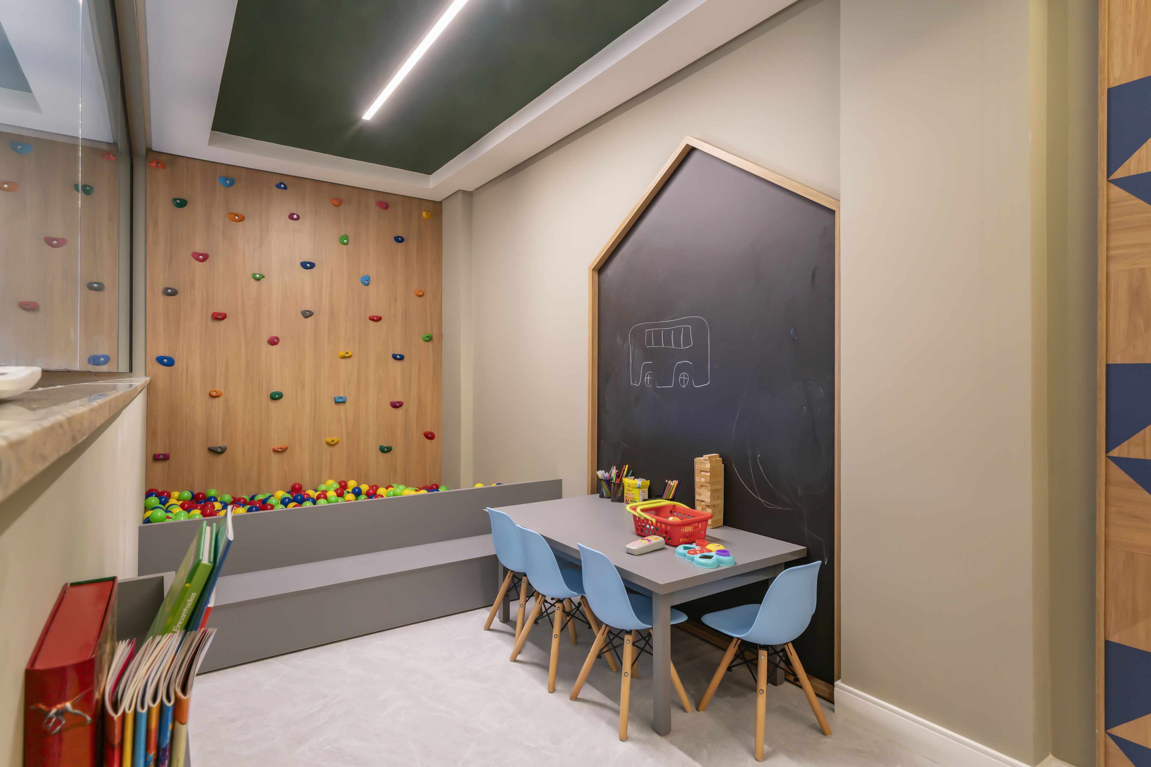 Ein Kinderspielzimmer mit Kletterwand, einer Tafel und einem Tisch mit Stühlen.