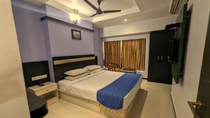 A bedroom with a bed, bedside tables, a desk, a chair, a ceiling fan, and a TV. - RBS Residency (Tiruchirappalli)
