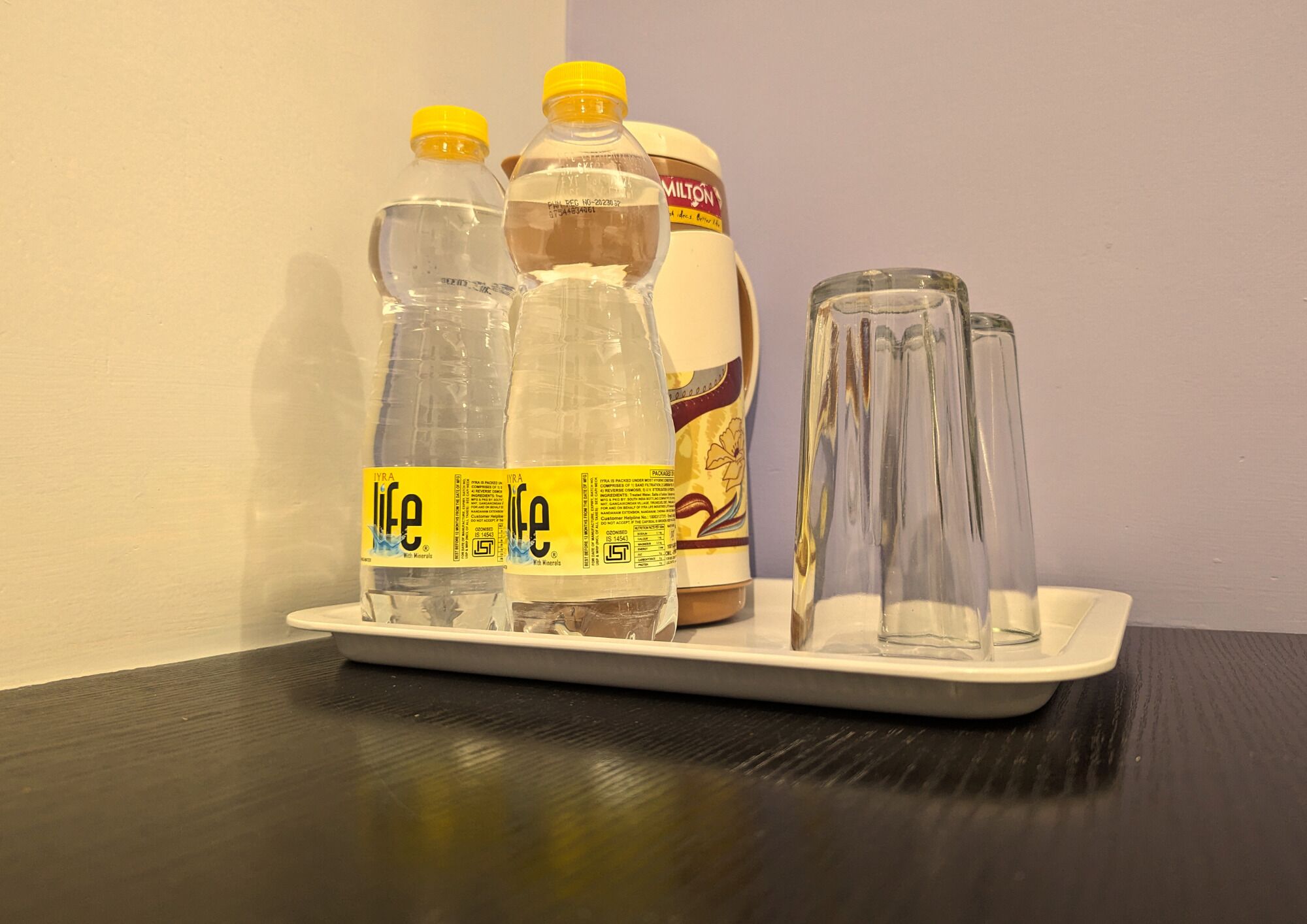 A tray with three water bottles and two glasses on a table.