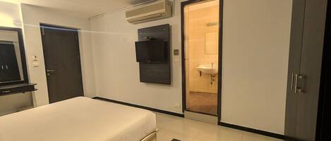 A bedroom with a bed, a TV mounted on the wall, an air conditioning unit, and a door leading to a bathroom.