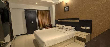 A hotel room with a bed, bedside tables, a desk, a chair, a ceiling fan, a door, and a wall-mounted light.