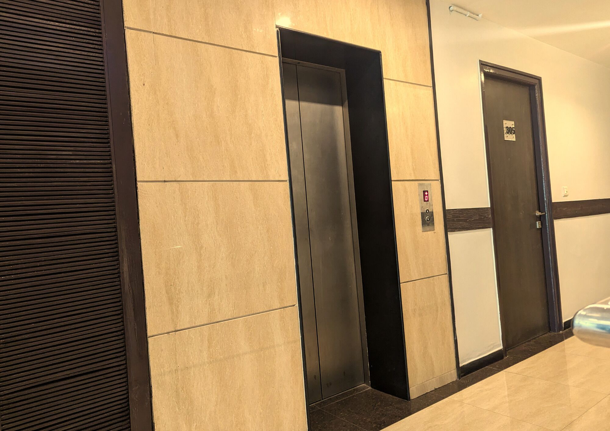 Un ascensor con detalles metálicos, una puerta con placa de número y un panel de madera horizontal en la pared.