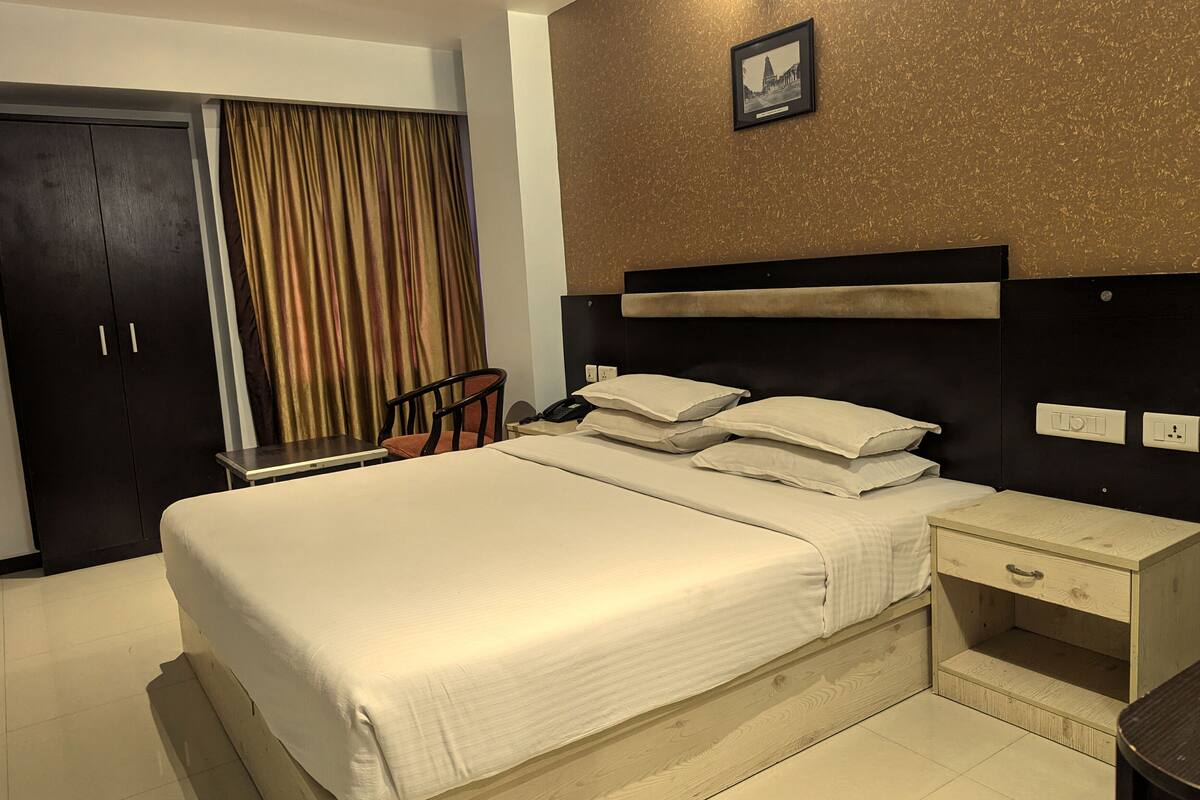 Ein Hotelzimmer mit einem großen Bett, einem Holfnachtkästchen, einem Sessel, einem Schreibtisch und einem Kleiderschrank.