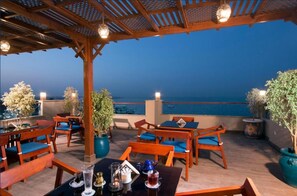A rooftop terrace with wooden furniture, potted plants, and a view of the sea.