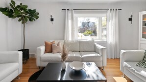 A modern living room with a white sofa, a coffee table, and a large window with curtains. - Enjoy a stylish experience at this fresh and clean  lower apartment!  This place is newly renovated and perfect for a stay in the Metro Detroit. It's located near the Detroit Zoo right by major highways. This home is a duplex building and includes 2 (Oak Park)