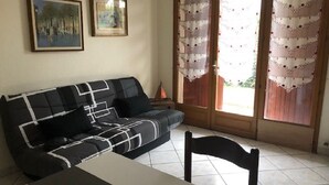 Un salon avec un canapé noir et blanc, une table à manger et des chaises. Deux tableaux encadrés ornent le mur, et une porte-fenêtre à glissière est agrémentée de rideaux.