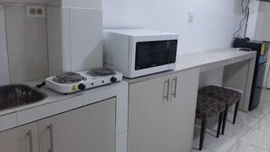 Eine kleine Küche mit Mikrowelle, Gasherd und einem kleinen Hocker.