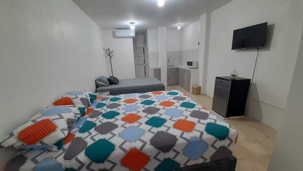 Ein Schlafzimmer mit Bett, Fernseher, Schreibtisch und einer Küchenzeile.