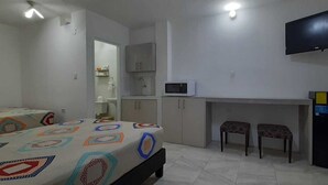 Ein Schlafzimmer mit zwei Betten, einem Schreibtisch mit Stuhl, einem Fernseher und einem Kühlschrank.