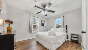 A bedroom with a bed, a ceiling fan, a nightstand, a vase with flowers, and a window.