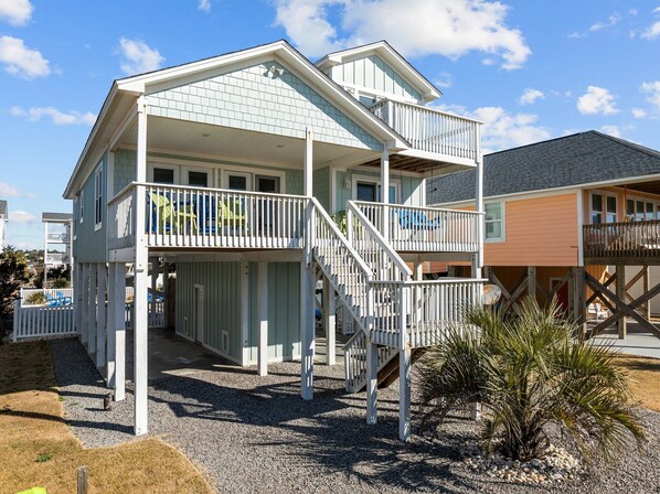 A two-story beachfront house with a covered porch and a balcony.