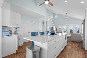 A spacious kitchen with white cabinetry, a large island, and a ceiling fan.