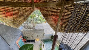 A view from a high vantage point inside a building with a thatched roof, a stone wall, and a small pool area. - Happiness Kulambo Villa El Nido (El Nido)