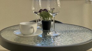 Una mesa redonda de vidrio con dos copas de vino, una taza blanca y una pequeña planta en maceta.