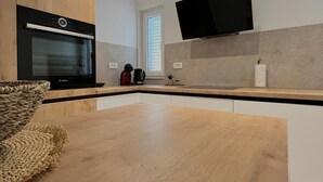 Una cocina moderna con horno empotrado, televisor de pantalla plana sobre la encimera y un amplio ventanal que proporciona luz natural.