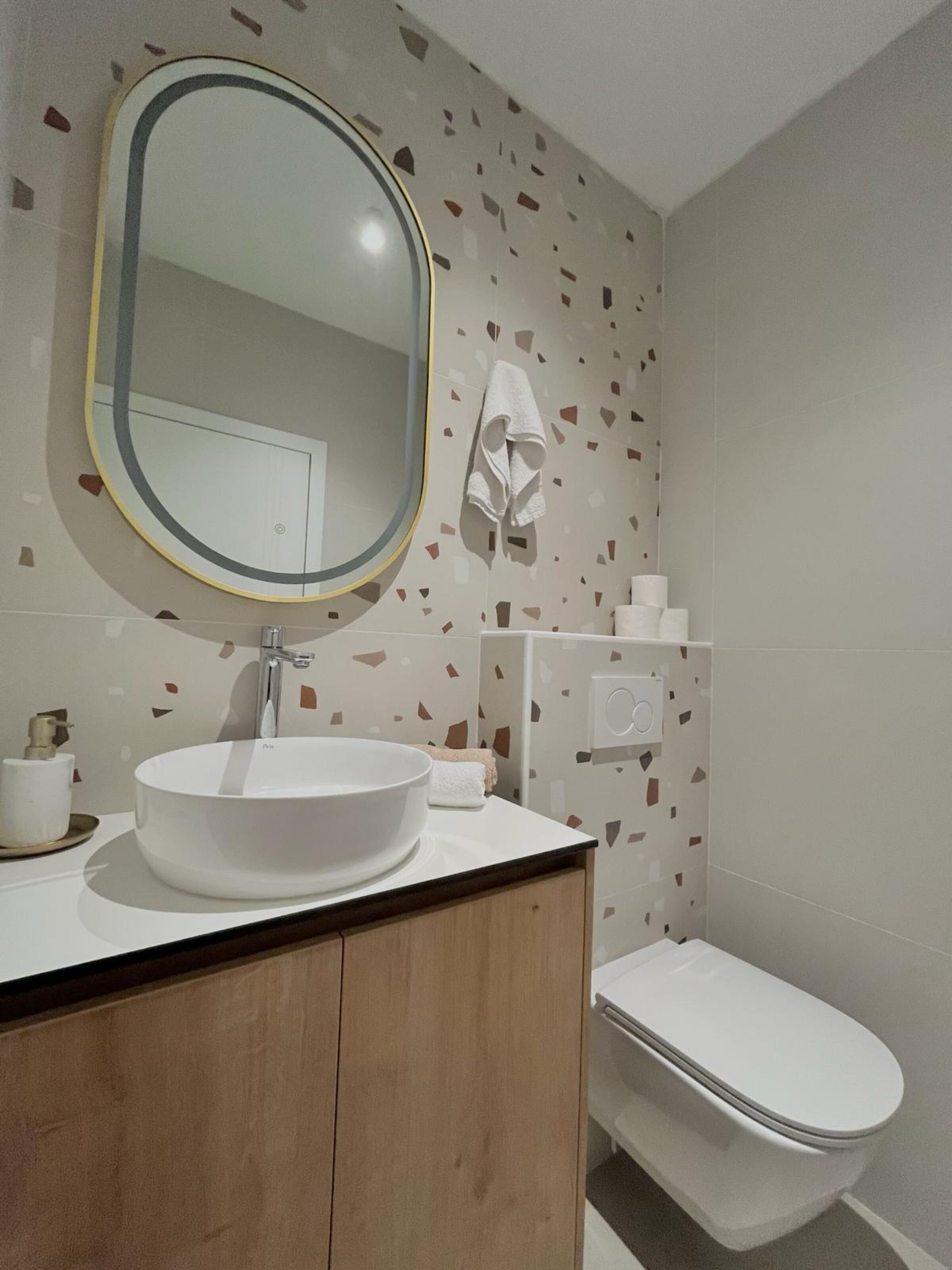 Un baño moderno con un espejo redondo, lavamanos blanco y retrete.