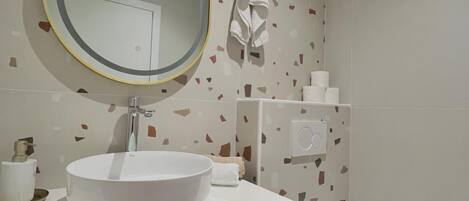Un baño moderno con un espejo redondo, lavamanos blanco y retrete.