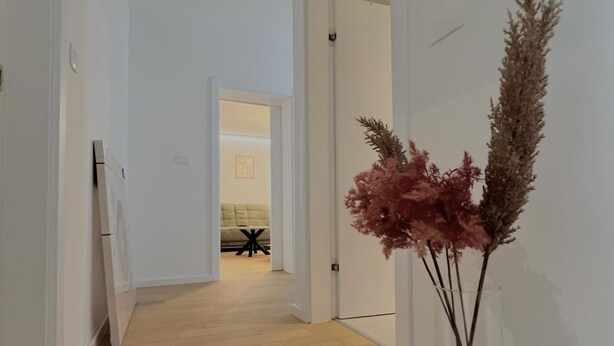 Un pasillo con suelo de madera, paredes blancas y vista despejada a otra habitación con una mesa y sillas.