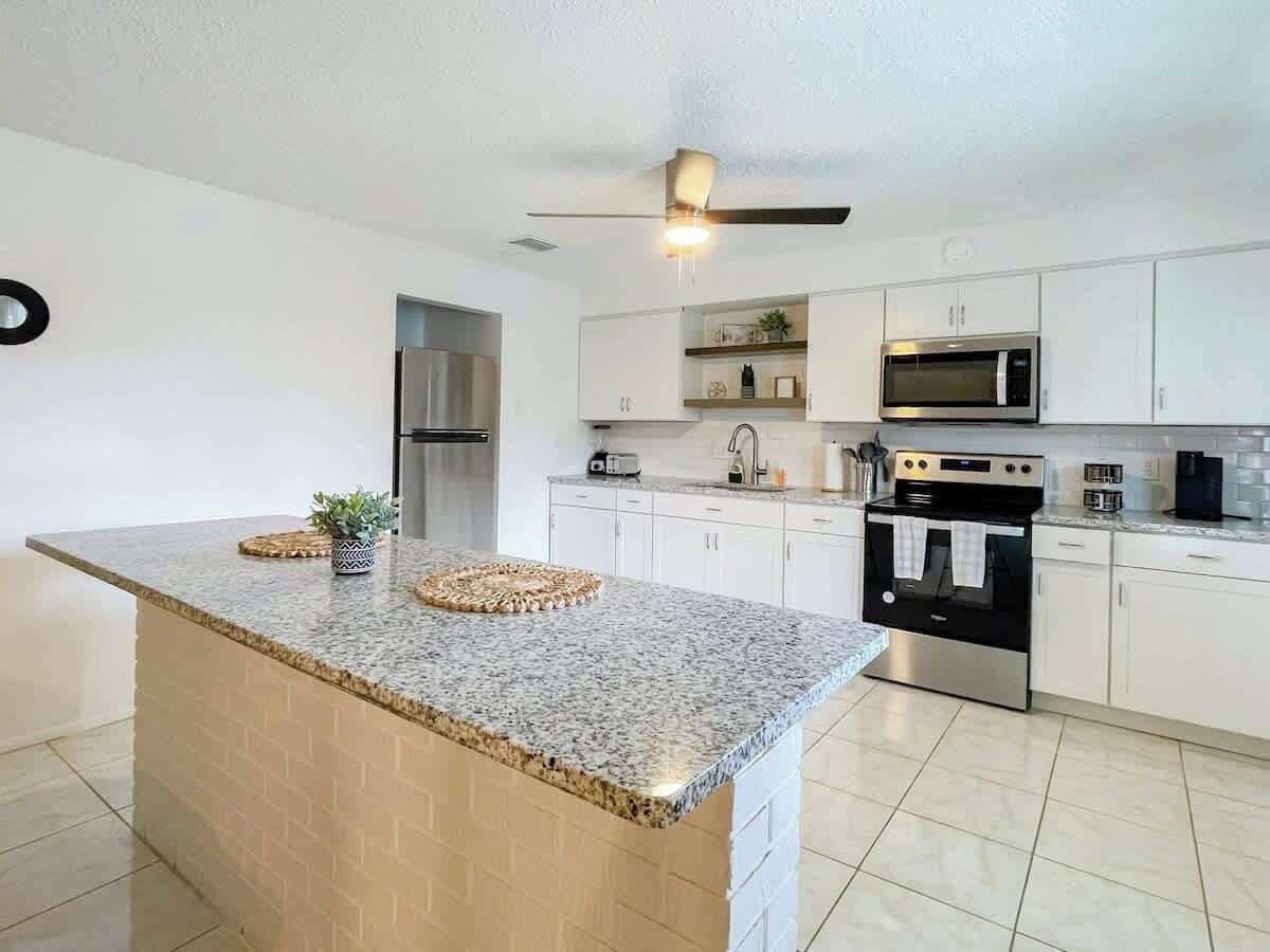 Una cocina moderna con encimeras de granito, electrodomésticos de acero inoxidable y armarios blancos.