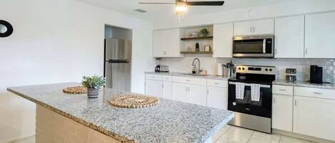 Una cocina moderna con encimeras de granito, electrodomésticos de acero inoxidable y armarios blancos.
