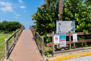 A wooden boardwalk leading to a beach area with palm trees and a clear sky. - Fillmore Unit 14 (Cape Canaveral)