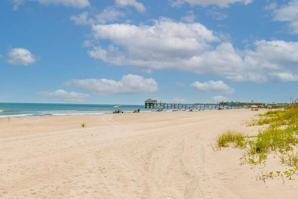 A beach with a pier extending into the ocean, a small building near the water, and clear skies.