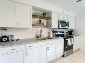A modern kitchen with white cabinets, a granite countertop, a built-in microwave, a stove, and a sink.