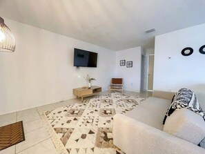Un salon moderne avec un téléviseur à écran plat fixé au mur, un tapis à motifs, un canapé et une table d’appoint en bois sur laquelle est posé un vase.