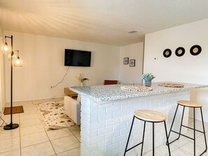 A kitchen with a white brick island, two bar stools, a flat-screen TV, and a floor lamp.