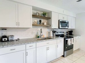 A modern kitchen with white cabinets, a granite countertop, a microwave, a stove, and a sink.