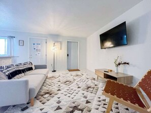 Ett vardagsrum med en soffa, ett soffbord, en tv som är monterad på väggen och en mönstrad matta.