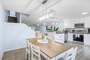 A modern kitchen with white cabinets, stainless steel appliances, and a wooden dining table.